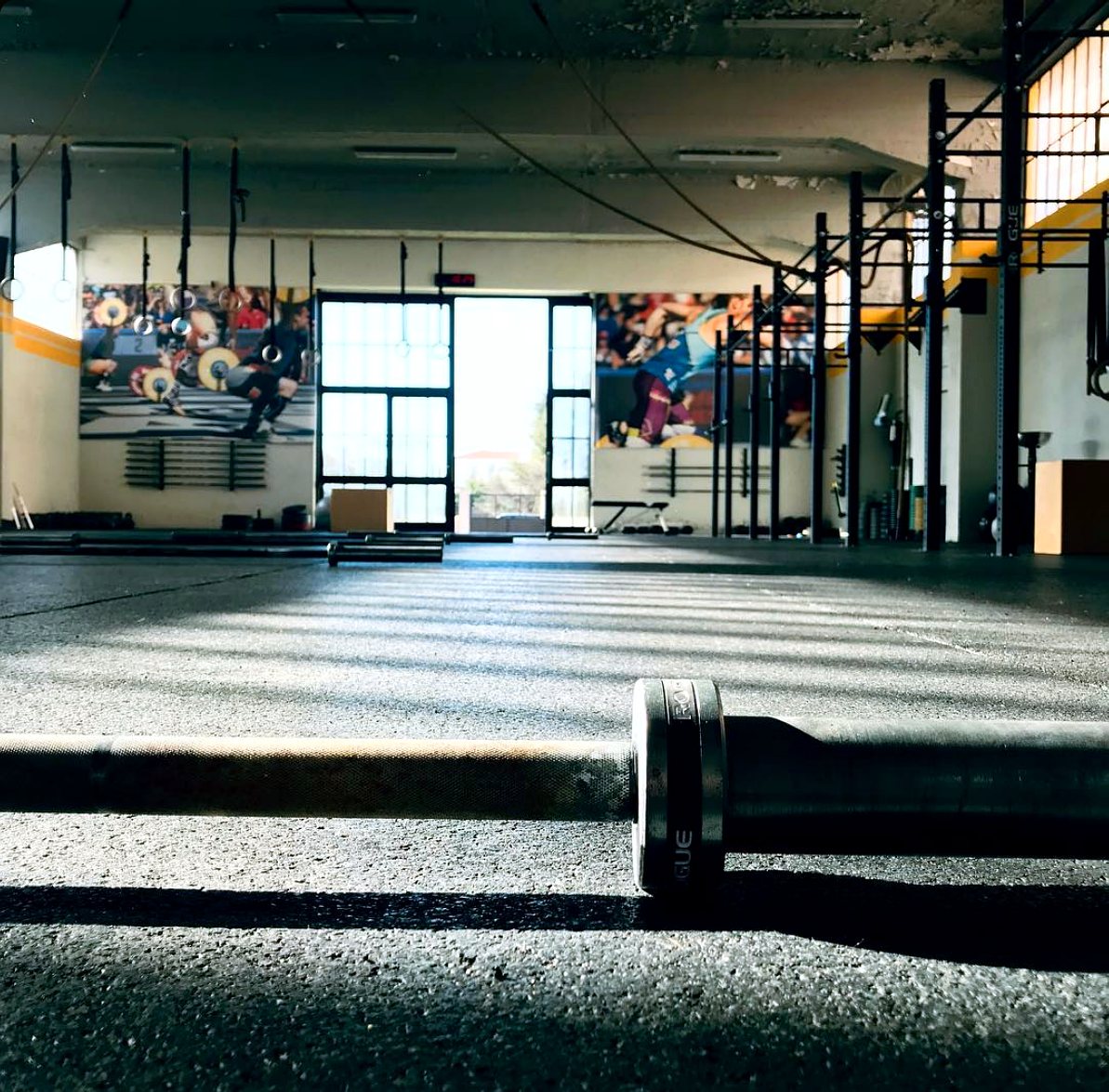 A barbell on the training floor at Campus Kifissia, with the rig and competition murals behind
